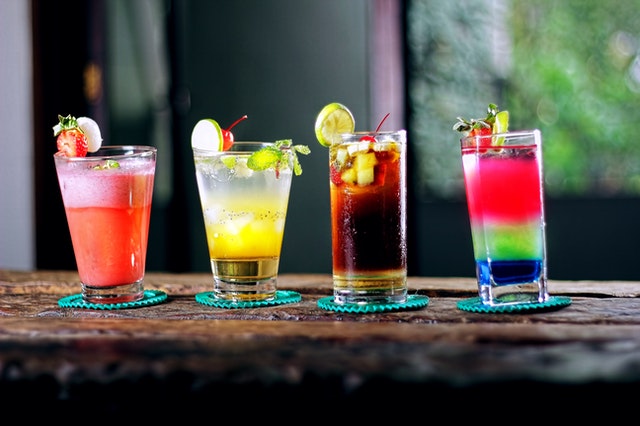 four colorful drinks in glasses on brown wooden surface