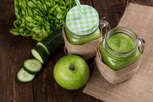 green apple and sliced cucumber beside two clear mason jars with green colored drinks