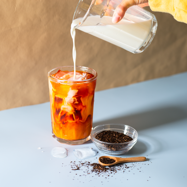 person pouring milk into a glass of Thai Tea made from Tea Zone Thai Tea Leaves