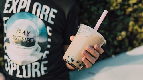 person in a black shirt holding boba tea with pink straw